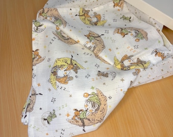 May include: A white muslin baby blanket featuring a repeating pattern of sleeping children on crescent moons and stars. The children are wearing pyjamas and have sleepy eyes. The blanket is soft and cuddly, ideal for a baby's nursery.