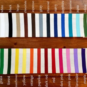 K&ouml;nnte beinhalten: Eine Sammlung von Stoffmustern in verschiedenen Farben, darunter Wei&szlig;, Schwarz, Beige, Schokolade, Espresso, Grau, Anthrazit, Marineblau, Saphir, T&uuml;rkis, Aqua, Oliv, Gras, Wald, Sonnenblume, Gelb, Orange, Paprika, Dunkelrot, Rot, Dunkelrosa, Hellrosa, Lavendel und Lila.