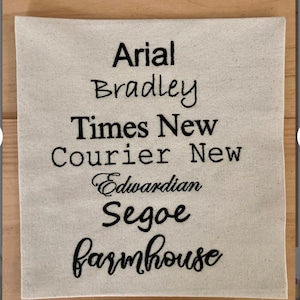 May include: A white fabric swatch with different font names embroidered in black thread. The fonts include Arial, Bradley, Times New Roman, Courier New, Edwardian Script ITC, Segoe Script, and Farmhouse.