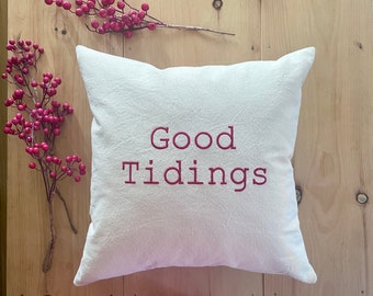 May include: White pillow with the text "Good Tidings" embroidered in red.