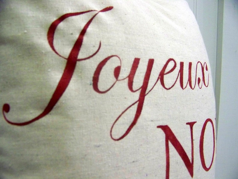 K&ouml;nnte beinhalten: Eine wei&szlig;e Stofftasche mit den Worten "Joyeux Noel" in roter Kursivschrift.