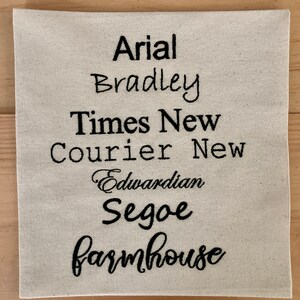 May include: A white fabric swatch with the names of different fonts embroidered in black thread: Arial, Bradley, Times New, Courier New, Edwardian, Segoe, and Farmhouse.