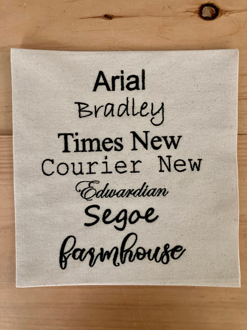 May include: A white fabric swatch with the names of different fonts embroidered in black thread: Arial, Bradley, Times New, Courier New, Edwardian, Segoe, and Farmhouse.