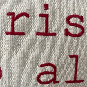 May include: Close-up of a white fabric pillow with red embroidered text that reads "Christmas to all".