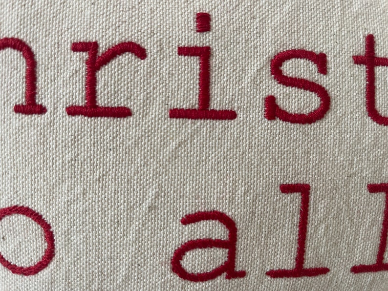 May include: Close-up of a white fabric pillow with red embroidered text that reads "Christmas to all".
