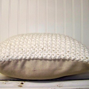 May include: White crocheted pillow with a beige linen backing. The pillow is made with a chunky yarn and has a textured surface.