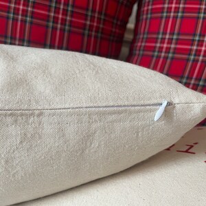 May include: A close-up of a beige pillow with a white zipper. The pillow is made of a soft, textured fabric.