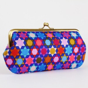 May include: A colorful clutch with a brass clasp. The fabric features a geometric pattern of blue, pink, red, yellow, and purple star shapes. The clutch is a rectangular shape with rounded edges.