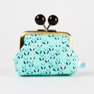 Può includere: Un piccolo porta monete blu turchese con una cornice dorata e chiusure a bottone nere. Il porta monete è decorato con un motivo ripetuto di orsi panda bianchi su uno sfondo blu turchese.