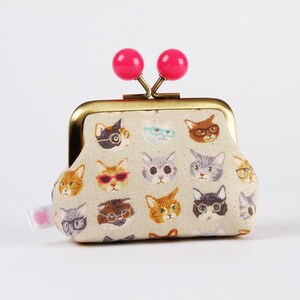 May include: A small, beige coin purse with a gold metal frame and pink plastic clasps. The purse is covered in a pattern of cats wearing glasses.