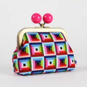 May include: A patterned coin purse with a gold-coloured frame and clasp. The fabric displays a geometric design in red, blue, green, and pink. Two bright pink spheres are on top of the clasp.