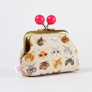 May include: A small beige fabric coin purse with a gold metal frame and pink plastic clasps. The purse is decorated with a repeating pattern of cats wearing glasses.