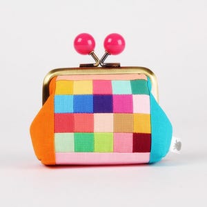 Peut inclure: Un porte-monnaie coloré avec un fermoir en laiton et deux accents sphériques roses. Le sac à main présente un motif patchwork de différentes couleurs, dont l'orange, le rose, le bleu, le vert et le rouge. Le design est un accessoire vibrant et accrocheur.
