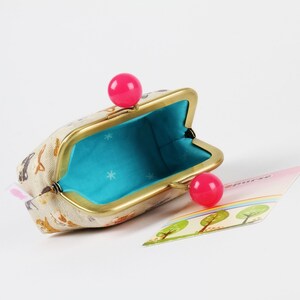 May include: A small, beige coin purse with a gold frame and pink plastic clasps. The purse is open and the inside is lined with a turquoise fabric with white stars.