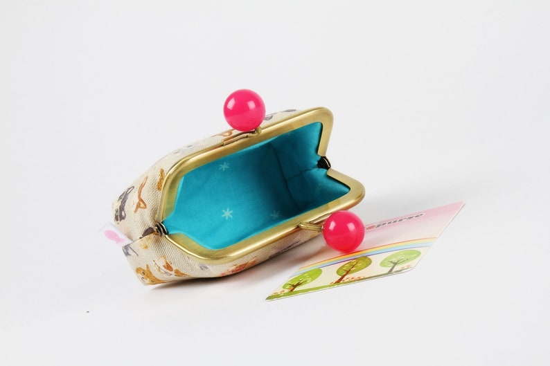 May include: A small, beige coin purse with a gold frame and pink plastic clasps. The purse is open and the inside is lined with a turquoise fabric with white stars.