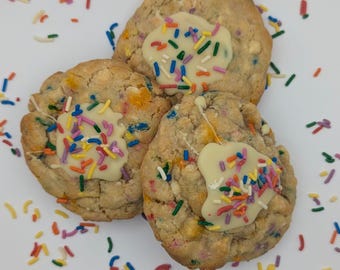 May include: Three white chocolate chip cookies with colorful sprinkles on a white plate. The cookies are topped with white chocolate frosting and more sprinkles.