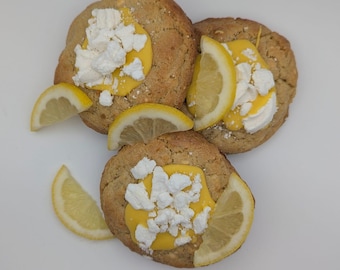 May include: Three lemon cookies with yellow icing and white meringue topping. The cookies are on a white surface.