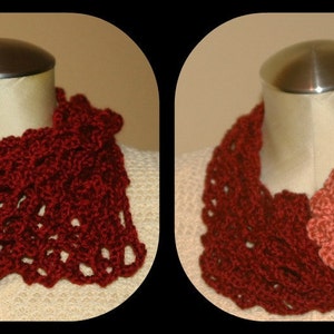 May include: A burgundy crocheted cowl with a delicate openwork pattern. The cowl is displayed on a mannequin and features a pink crocheted flower with a pearl button in the center.
