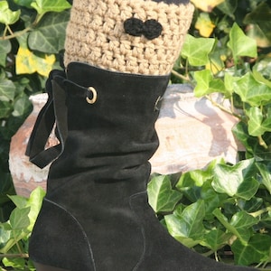 Puede incluir: Bota de tobillo de ante negro con tacón de cuña bajo. La bota se combina con un calentador de piernas de ganchillo color beige con un lazo negro. El fondo presenta hiedra verde.