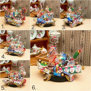 Könnte beinhalten: Ein Miniatur-Weihnachtswagen voller verpackter Süßigkeiten, Lollis und Pralinen. Der Wagen ist mit Weihnachtsmann-Gesichtern und goldenen Details verziert und sorgt für eine festliche Präsentation.