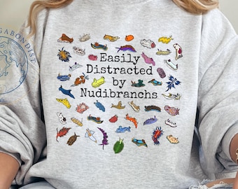 May include: Ash gray sweatshirt with the text "Easily Distracted by Nudibranchs" and colorful illustrations of nudibranchs. The sweatshirt features a crew neck and long sleeves. The Vagabondist logo is visible on the left side.