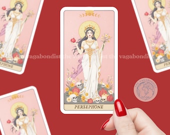 Op de afbeelding: Een rechthoekige sticker met een illustratie van Persephone op een lichtroze achtergrond. Ze draagt een wit gewaad, houdt een granaatappel en bloemen vast en staat tussen schedels en bloesems. De naam PERSEPHONE staat onderaan.
