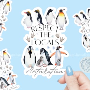 May include: A die-cut sticker featuring various watercolor penguins, snowflake icons, and the black text "RESPECT THE LOCALS" and "Antarctica". The design includes multiple penguin species in black, white, yellow, and orange, arranged around the text.