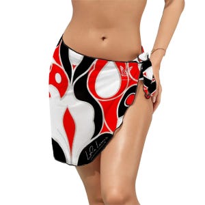 May include: A sarong with a bold, abstract design in red, black, and white. The fabric is tied at the hip, showcasing a vibrant pattern with curved lines and shapes. The sarong features the signature "Le Leux" in script.