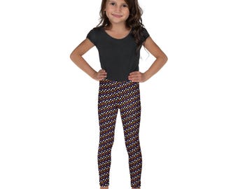 May include: A young girl in a black top and patterned leggings. The leggings have a repeating pattern of white, orange, and purple dots on a dark purple background. The girl is standing with her hands on her hips.