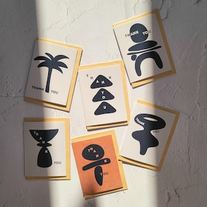 Könnte beinhalten: Eine Sammlung von Dankeskarten mit abstrakten schwarzen Designs auf weißem Hintergrund. Auf jeder Karte steht "THANK YOU". Die Karten befinden sich in hellfarbigen Umschlägen.