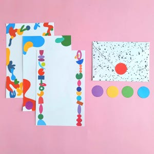 Peut inclure: Un ensemble de papeterie avec du papier blanc orné de motifs abstraits colorés, une enveloppe avec des mouchetures noires et un cercle rouge, et quatre autocollants circulaires colorés. Le fond est rose uni.