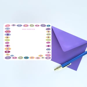 Peut inclure: Une carte de correspondance rectangulaire blanche avec une bordure d'icônes en forme d'œil colorées dans des tons de rose, bleu, vert et violet. Le nom ANNE HARRISON est imprimé en rose au centre. Une enveloppe violette et un stylo bleu sont inclus.