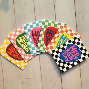 May include: A collection of colorful birthday cards with a checkerboard pattern. Each card features a different color scheme, including yellow, brown, green, pink, red, orange, blue, and black, with the words "Happy Birthday" in a unique font.