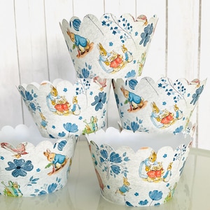May include: Set of six white cupcake liners with a scalloped edge. The liners feature a blue and white floral pattern with illustrations of Peter Rabbit and his friends.