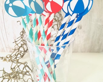 May include: A glass filled with red, blue, and turquoise striped paper straws with blue and red beach ball cutouts attached to the ends.