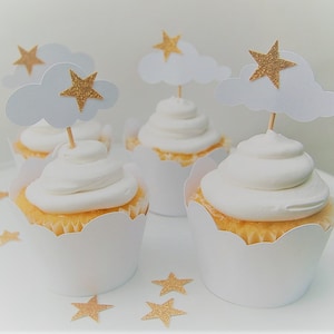 May include: Four white cupcakes with white frosting and gold glitter star toppers. The toppers are on a white cloud with a gold glitter star.