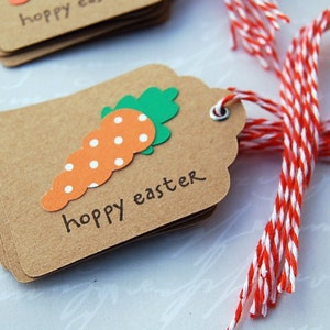 May include: A stack of brown gift tags with a white string attached. The tags are decorated with a paper carrot with white polka dots and green leaves. The text "happy easter" is written on the tag.