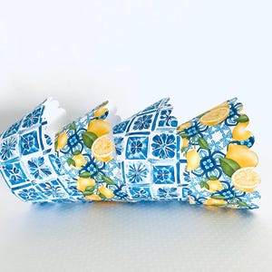 May include: Decorative paper crown featuring a blue and white tile pattern with yellow lemons and green leaves. The crown has a scalloped edge and is designed to be worn. The design is reminiscent of Mediterranean decor.