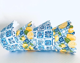 May include: Decorative paper crown featuring a blue and white tile pattern with yellow lemons and green leaves. The crown has a scalloped edge and is designed to be worn. The design is reminiscent of Mediterranean decor.