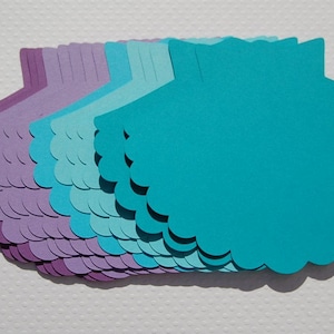 May include: A stack of scalloped paper shapes in shades of purple and blue. The shapes are layered with the largest on top and the smallest on the bottom.