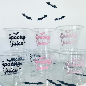 May include: Six clear plastic cups with the text "Spooky Juice" in black and pink lettering. The cups are decorated with small bat silhouettes.