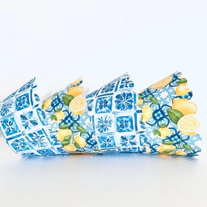 May include: Decorative paper crown with a blue and white tile pattern and lemon illustrations. The crown is made of folded paper and has a scalloped edge. The lemons are yellow with green leaves.
