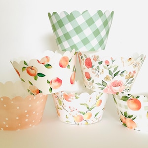 May include: A stack of six decorative cupcake liners. The liners feature various designs, including peach and floral patterns, a light green gingham check, and a peach polka dot design. The liners have a scalloped edge.