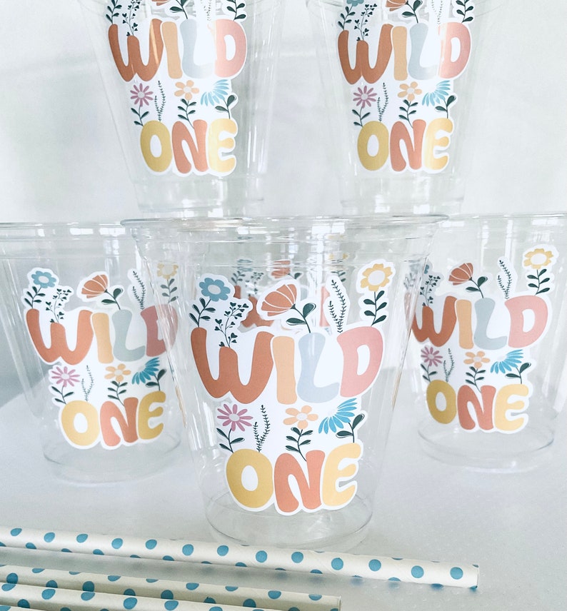 May include: Set of six clear plastic cups with floral and leafy designs and the text "Wild One" in a colorful, retro font. The cups are perfect for a first birthday party.