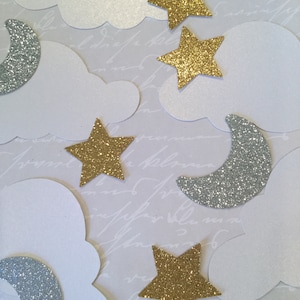 May include: A collection of white clouds, silver glitter moons, and gold glitter stars. The stars and moons are cut out of paper and have a sparkly finish.