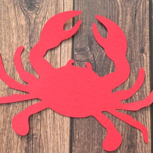 May include: Red paper cutout of a crab on a wood background.