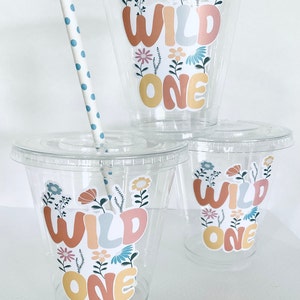 May include: Three clear plastic cups with lids and straws. Each cup has a colorful sticker with the words "Wild One" and floral designs.