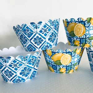 May include: A collection of decorative cupcake liners. Some liners feature a blue and white geometric pattern, while others display lemons with green leaves against a blue and white background. The liners have a scalloped edge.