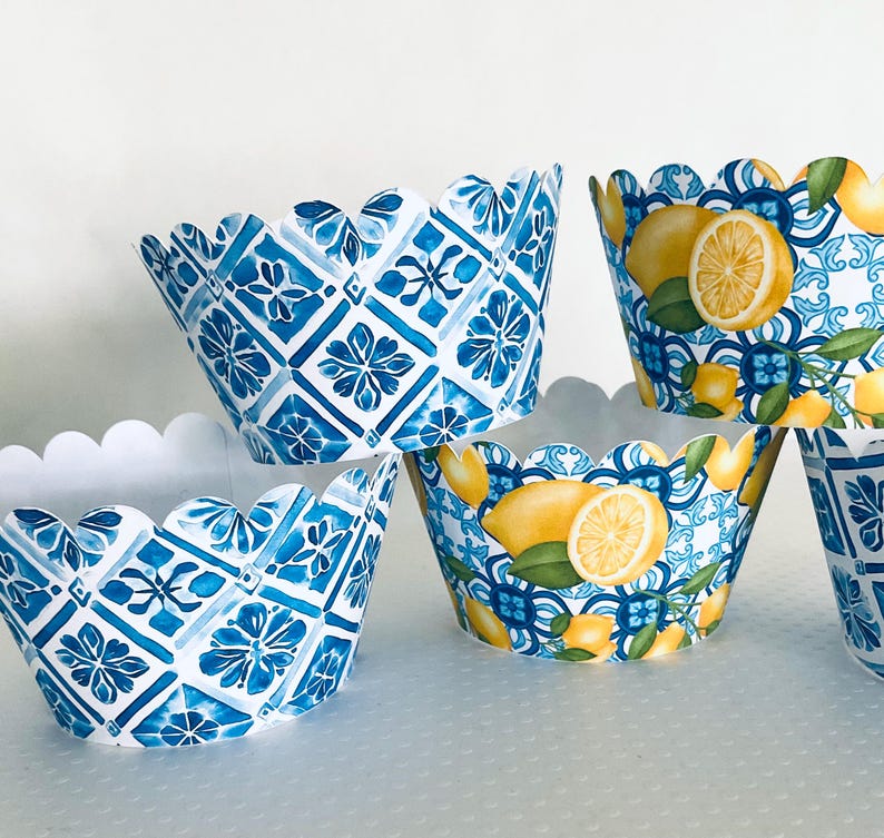 May include: A collection of decorative cupcake liners. Some liners feature a blue and white geometric pattern, while others display lemons with green leaves against a blue and white background. The liners have a scalloped edge.