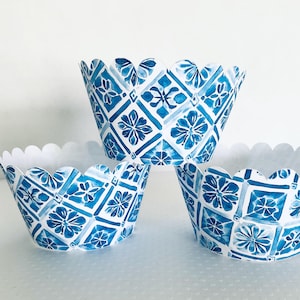 May include: Three blue and white patterned cupcake liners with a scalloped edge. The design features a floral and geometric pattern in shades of blue on a white background. The liners are stacked on top of each other.